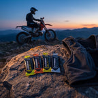 Cuatro Evoenergy gel sin cafeína sobre una roca al atardecer junto a un chaleco de hidratación