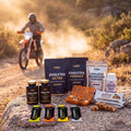 Pack RUTA XL: los cuatro Evolytes, los dos magnesios, las barritas de almendra, cuatro geles Evoenergy y el pastillero sobre una roca junto a una pista de enduro